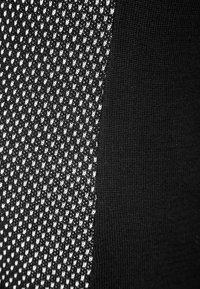 Svart tyg med ett strukturerat mönster har en stickad sektion till vänster, i kontrast till ett slätt svart område till höger.