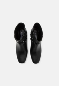 Black ankle boots made of smooth leather with a pointed toe, featuring a decorative strap with small metallic studs and a side zipper.