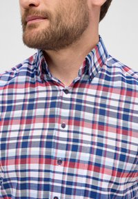 Camicia a quadri con colori rosso, blu e bianco. Collo button-down, maniche corte e bottoni rossi a contrasto sul davanti.