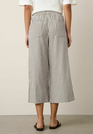 Person wearing black and white checkered wide-leg cropped pants and black open-back sandals, standing against a neutral background.