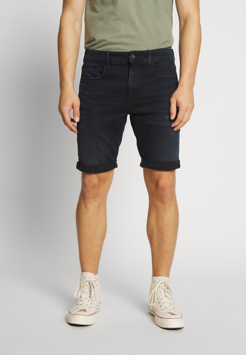 Mörka denimshorts med rullade nederkanter, som har en klassisk femfickedesign. Åtkomst tillsammans med en ljusgrön t-shirt och vita högsilhuett sneakers.