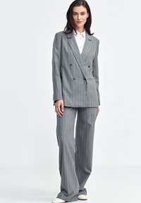 Szary marynarka w prążki w podwójnym rzędzie guzików z szerokimi klapami, dopasowane spodnie o szerokich nogawkach oraz jasnoróżowa koszula z kołnierzykiem pod spodem.