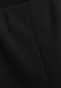 Sort stof med en glat tekstur, der har folder og et skræddersyet design. Minimalistisk stil med et klassisk udseende.