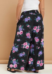 Svarta vida byxor med blommönster i rosa, lila och grönt. Har resårlinning och lös passform för komfort.