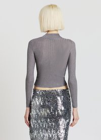 Graues, geripptes Langarmoberteil mit Stehkragen und figurbetonter Passform. Kombiniert mit einem silbernen Paillettenrock.