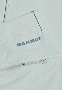 Ljusblå utomhusbyxor har en zip-fickor, reflekterande detaljer och förstärkt sömnad. Logotypen "Mammut" är framträdande på tyget.