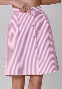 Jupe A-line rayée rose et blanche avec une taille haute, comportant trois boutons décoratifs et des poches avant. Texture de tissu lisse.