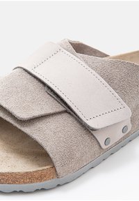 Gray suede sandal featuring a wide strap with a Velcro closure, padded footbed, and a textured rubber outsole.