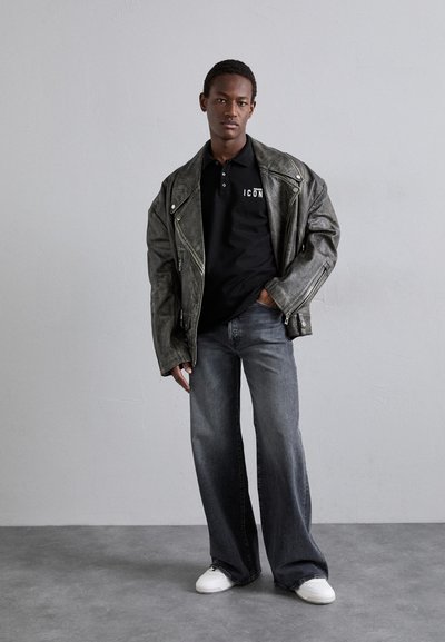 Schwarzes Poloshirt mit "ICON"-Logo, oversized graue Lederbikerjacke, weit geschnittene, verblasste graue Jeans und weiße Sneakers.