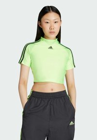 Neon vihreä lyhytnokkainen urheilu paita, jossa on lyhyet hihat, mustat korostusraidat ja Adidas-logo edessä, yhdistettynä mustiin housuihin.