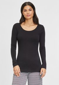 Schwarzes langärmliges Oberteil mit Rundhalsausschnitt und figurbetonter Silhouette, aus weichem Stoff, getragen mit gemusterten Hosen mit Zickzackdesign.
