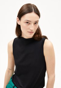 Top senza maniche nero con collo alto, realizzato in un tessuto liscio. Presenta un design minimale e una forma aderente.