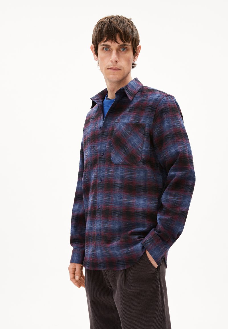 Geruite overhemd in marineblauw, bordeaux en grijs met een knoopsluiting aan de voorkant, een borstzak en een kraag. Gemaakt van een gestructureerde stof. Draagt over een blauw shirt.
