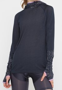 Dlouhý rukáv sportovní top v tmavě modré barvě se vzorovaným kapucí. Obsahuje otvory na palce a světle růžový lem na manžetách a spodním okraji.