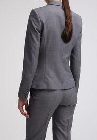 Grå skräddarsydd blazer med texturerad tyg, åtsittande design och knappdetaljer vid ärmarna, matchande byxor. Bakifrån visad.