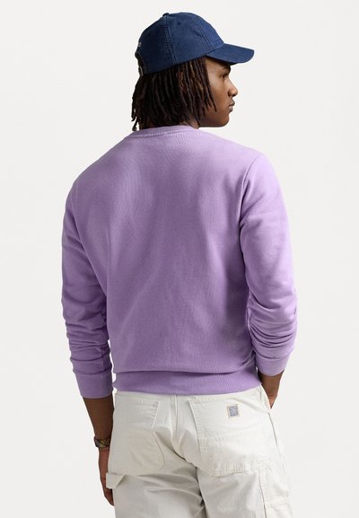 Sweatshirt leveiro lilás com punhos e bainha canelados, combinado com calças cargo de cor clara. A vista de costas mostra o decote redondo e o tecido texturizado.