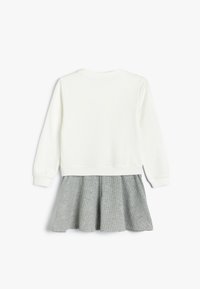 Hvid sweatshirt med lange ærmer, parret med en plisseret grå nederdel med et struktureret mønster. Simpel design uden udsmykninger.