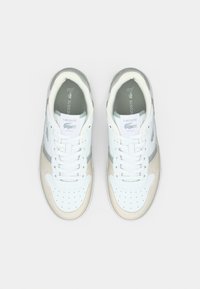 Αθλητικά παπούτσια Lacoste με άνω μέρος από λευκό δέρμα, γκρίζες λεπτομέρειες και τακούνι από μπεζ δέρμα. Διαθέτουν τρύπες αερισμού και λευκά κορδόνια.