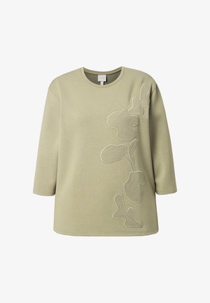 Długa koszula w kolorze jasnej oliwki z okrągłym dekoltem, ozdobiona wypukłą abstrakcyjną kwiatową haftowaną dekoracją wzdłuż prawej strony przodu.