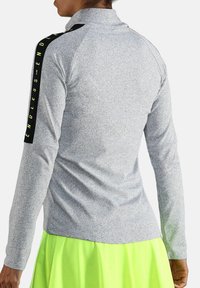 Grijze langemouwen shirt met een hoge kraag, voorzien van zwarte en neongele accenten langs de schouders en een gestructureerde afwerking.