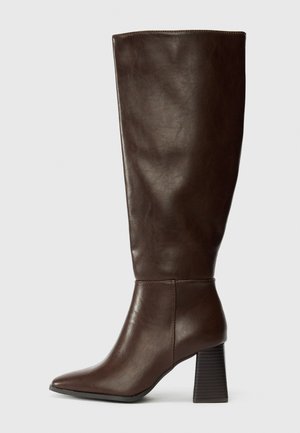 Bota de cuero marrón hasta la rodilla con puntera afilada y tacón grueso y texturizado. Acabado suave con detalles de costura mínimos.