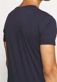 Tmavě modré tričko vyrobené z měkké látky, s krátkými rukávy a kulatým výstřihem. Zadní strana má hladký, nezdobený povrch.