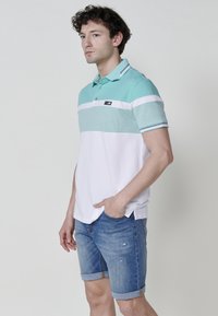 Menta zöld és fehér csíkos, galléros póló, sima pamutból készült, farmer rövidnadrággal párosítva. A mellkason márkás címke található.