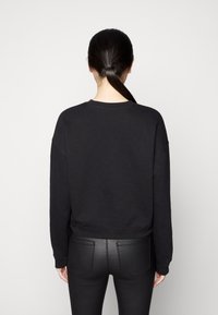 Sudadera negra con un corte relajado, cuello redondo y puños acanalados. El material parece suave; combinada con pantalones ajustados negros. Diseño minimalista.
