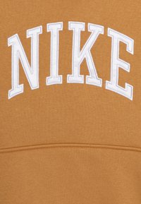 Brun sweatshirt med ordet "NIKE" i stora, vita, broderade versaler över bröstet. Mjuk, texturerad tyg.