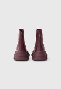 Bottes à la cheville bordeaux avec des zips à l'arrière, texture lisse, semelles en caoutchouc épaisses et forme arrondie.