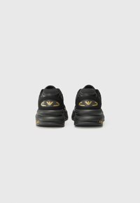Black athletic shoes with a textured upper, featuring gold logo accents, rounded heel, and rubber sole with grip patterns.