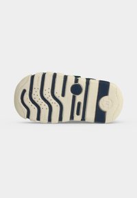 Semelle de chaussure en caoutchouc beige et bleu marine avec des motifs ondulés, des détails circulaires et un marquage de la taille, vue de dessous.
