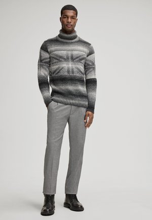 Maglione a collo alto con motivo a blocchi grigi e neri abbinato a pantaloni grigi chiari su misura e stivali stringati neri. Design e trama semplici.