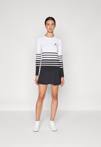 Vestido de baño de manga larga con rayas horizontales blancas y negras, que cuenta con una falda negra, cuello redondo y logotipo en el pecho. La tela es suave.