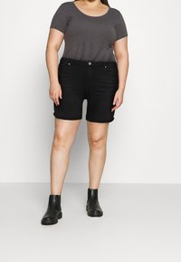 Černé džínové šortky s ohrnutým lemem, doplněné šedým krátkým tričkem. Modelka nosí černé kotníkové boty. Jednoduchý, neformální design.