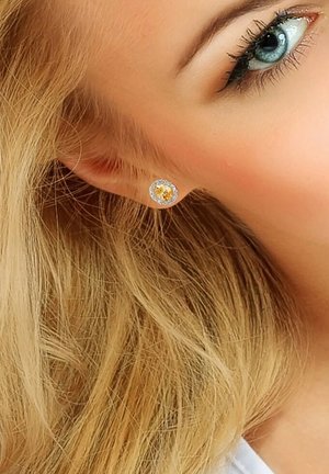 Boucles d'oreilles rondes présentant une pierre précieuse jaune centrale entourée d'accents clairs étincelants, montées dans un métal couleur argent.
