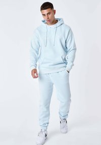 Lichtblauwe hoodie met kangoeroezak en trekkoorden, gecombineerd met bijpassende joggingbroek met een geborduurd logo, witte sneakers.