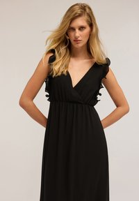 Schwarzes ärmelloses Kleid mit tiefem V-Ausschnitt und gerafften Akzenten an den Schultern. Weicher Stoff, geraffte Taille und fließende Silhouette.