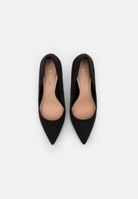 Zapatos de tacón de ante negro con punta afilada, forro interior suave, diseño minimalista y silueta elegante. Sin herrajes o acentos visibles.