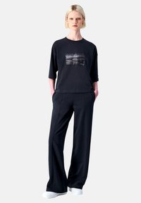 Schwarzes lässiges oversized T-Shirt mit grafischem Druck, kombiniert mit lockeren schwarzen Hosen. Das Material wirkt weich und eignet sich gut für entspannte Freizeitkleidung.