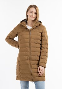 Bruine pufferjas met een capuchon, voorzien van een rits aan de voorkant en een geborduurd patroon, gecombineerd met lichtblauwe jeans.