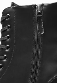 Botine din piele neagră, cu fermoar pe lateral, sireturi contrastante și ochiuri metalice. Textură netedă și cusături detaliate vizibile.