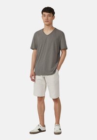 Grijze v-hals t-shirt, ontspannen pasvorm, gecombineerd met witte shorts. Model draagt witte sneakers met donkere accenten. Eenvoudig ontwerp, casual stijl.