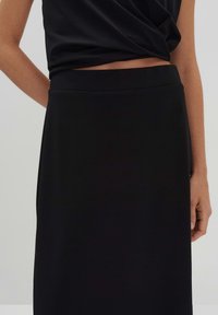 Jupe noire, longueur genoux, en tissu lisse. Présente une taille ajustée et une silhouette simple et épurée sans motifs ni embellissements.