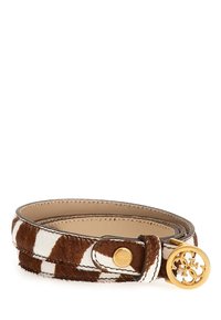 Cintura in pelliccia marrone e bianca con una forma liscia e arrotondata. Presenta una fibbia circolare dorata e una chiusura a bottone a scatto. Texture morbida.