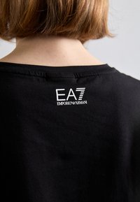 Čierne bavlnené tričko s okrúhlym výstrihom a krátkymi rukávmi. Na zadnej strane sa nachádza biele logo EA7 Emporio Armani. Mäkkučký materiál.