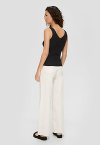 Czarny prążkowany top na ramiączkach z dekoltem w serek, zestawiony z szerokimi kremowymi spodniami i czarnymi sandałami, widok z tyłu ukazujący dopasowanie stroju.