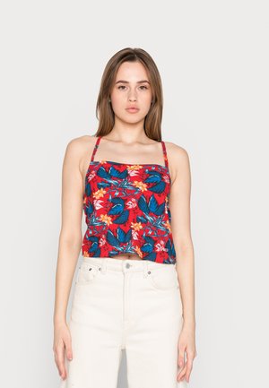 Top corto rojo con estampado floral en azul y amarillo, tirantes finos tipo espagueti y escote cuadrado, combinado con unos jeans blancos de cintura alta.