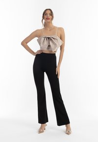 Beige satijnen cropped top met grote strikdetail, gecombineerd met hoge, rechte zwarte flared broeken en transparante hakken.
