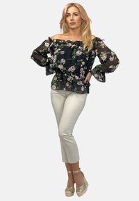 Czarna kwiecista bluzka bez ramiączek z przezroczystymi długimi rękawami i falbaniastym dołem, połączona z jasnobeżowymi spodniami o długości 3/4 i złotymi espadrylami na koturnie.